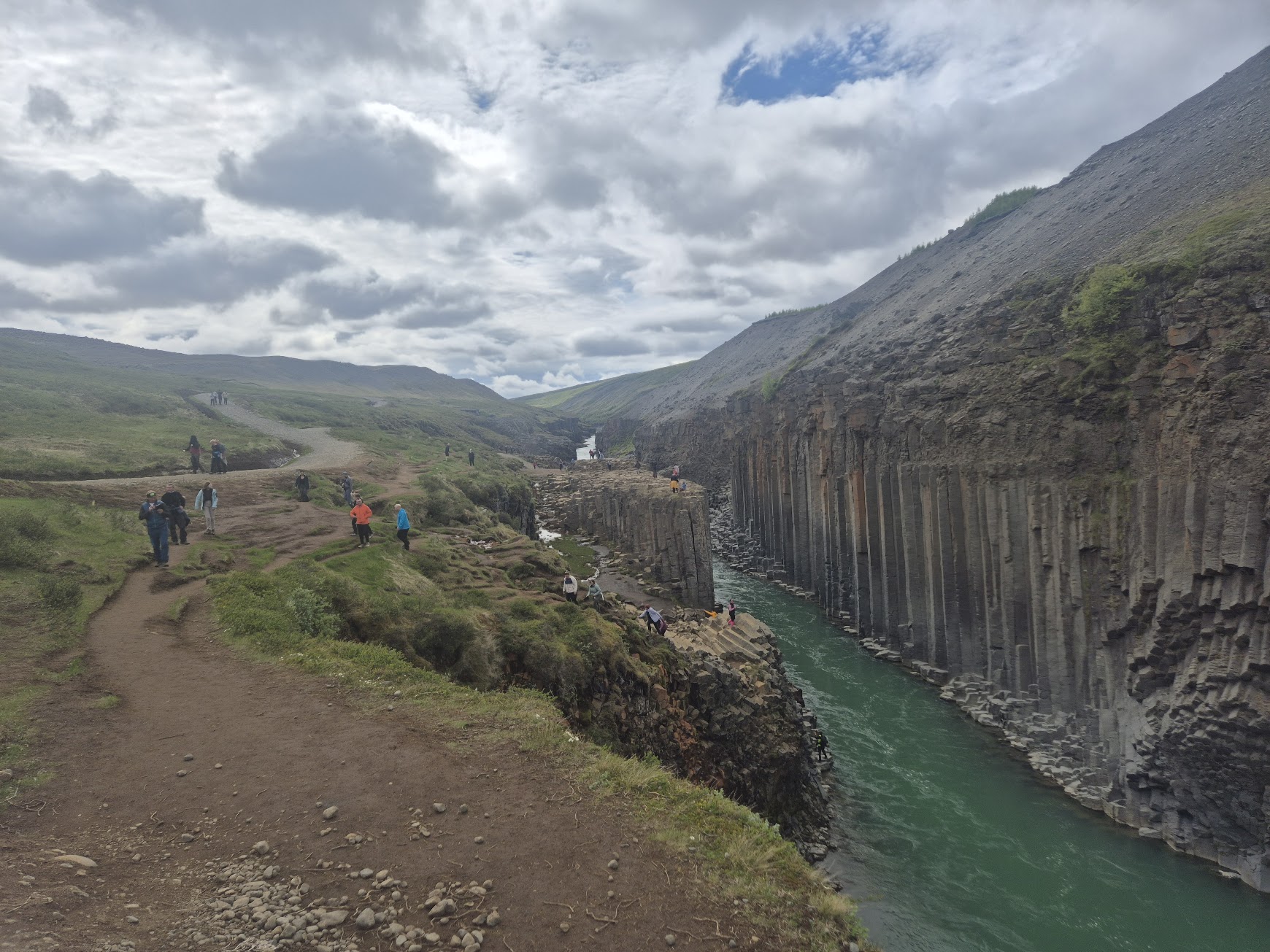 Visitors walking the upper path above Stuðlagil canyon's basalt columns