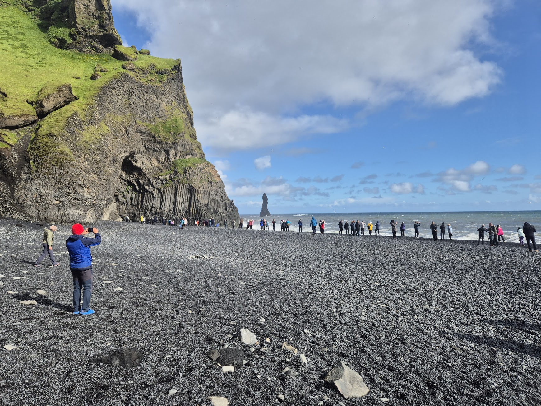 Visitors at Reynisfjara below the basalt cliffs with Reynisdrangar sea stack