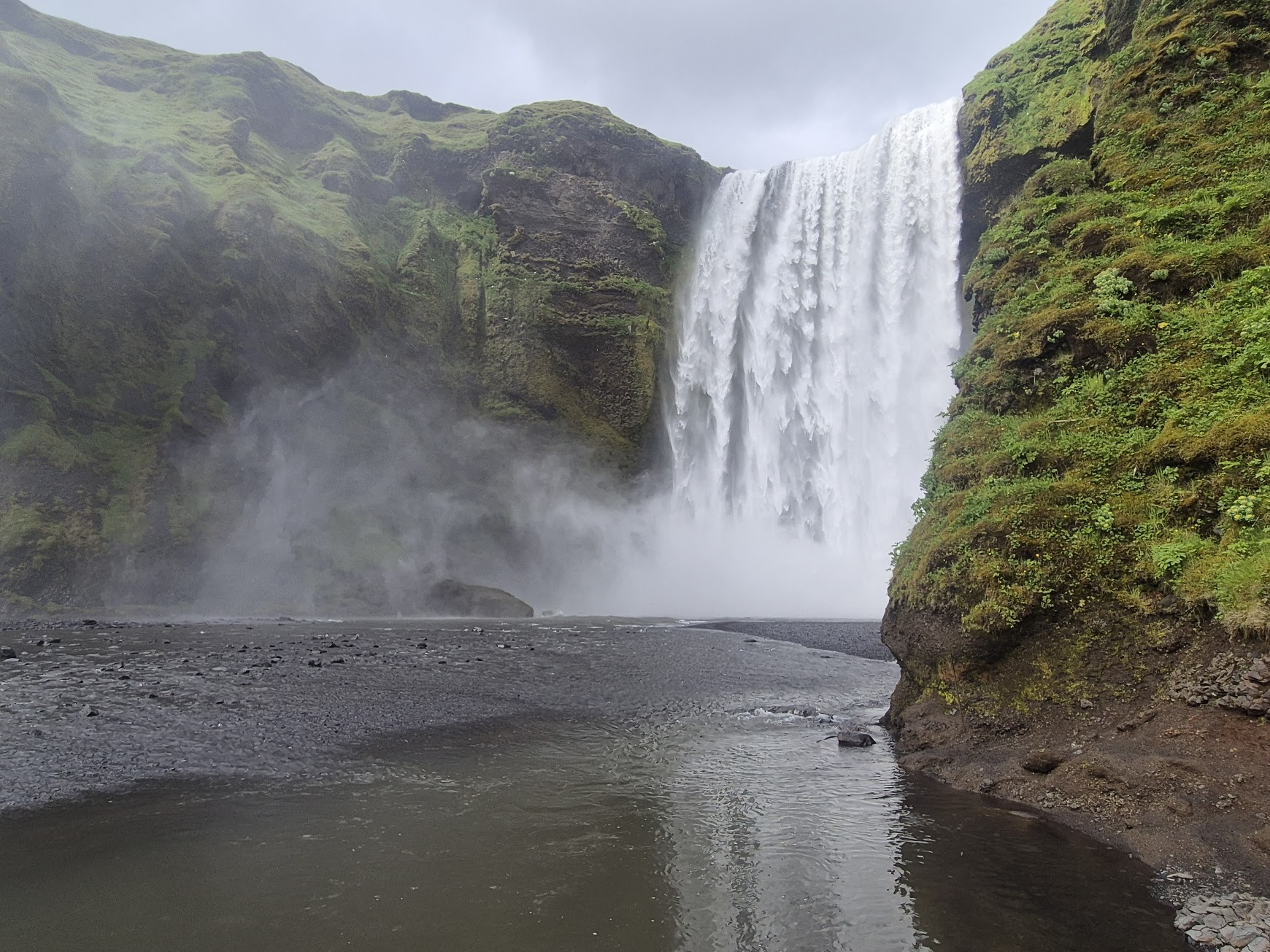 Close view of Skógafoss waterfall with mist rising from the black sand base