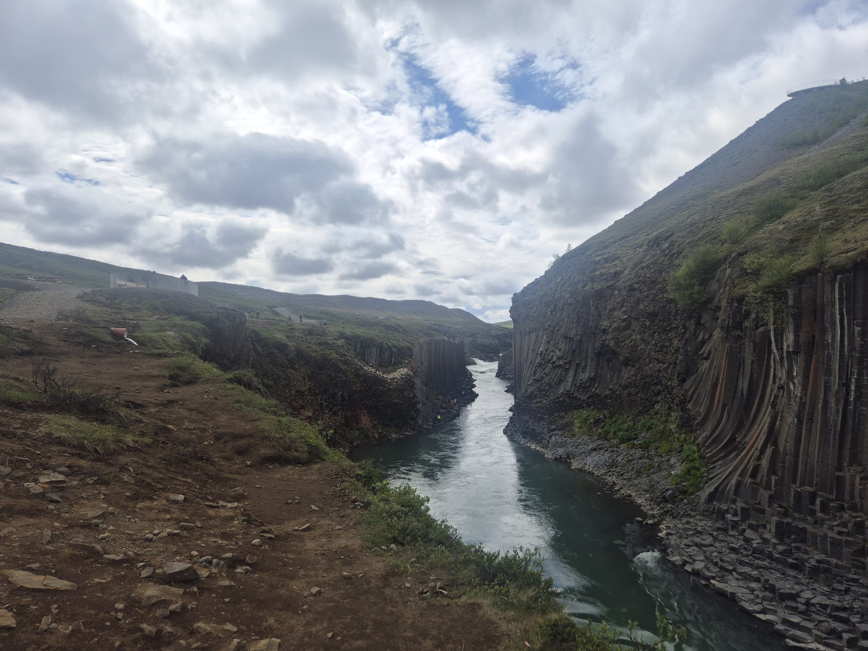 Stuðlagil canyon basalt columns rising above the river under cloudy summer skies