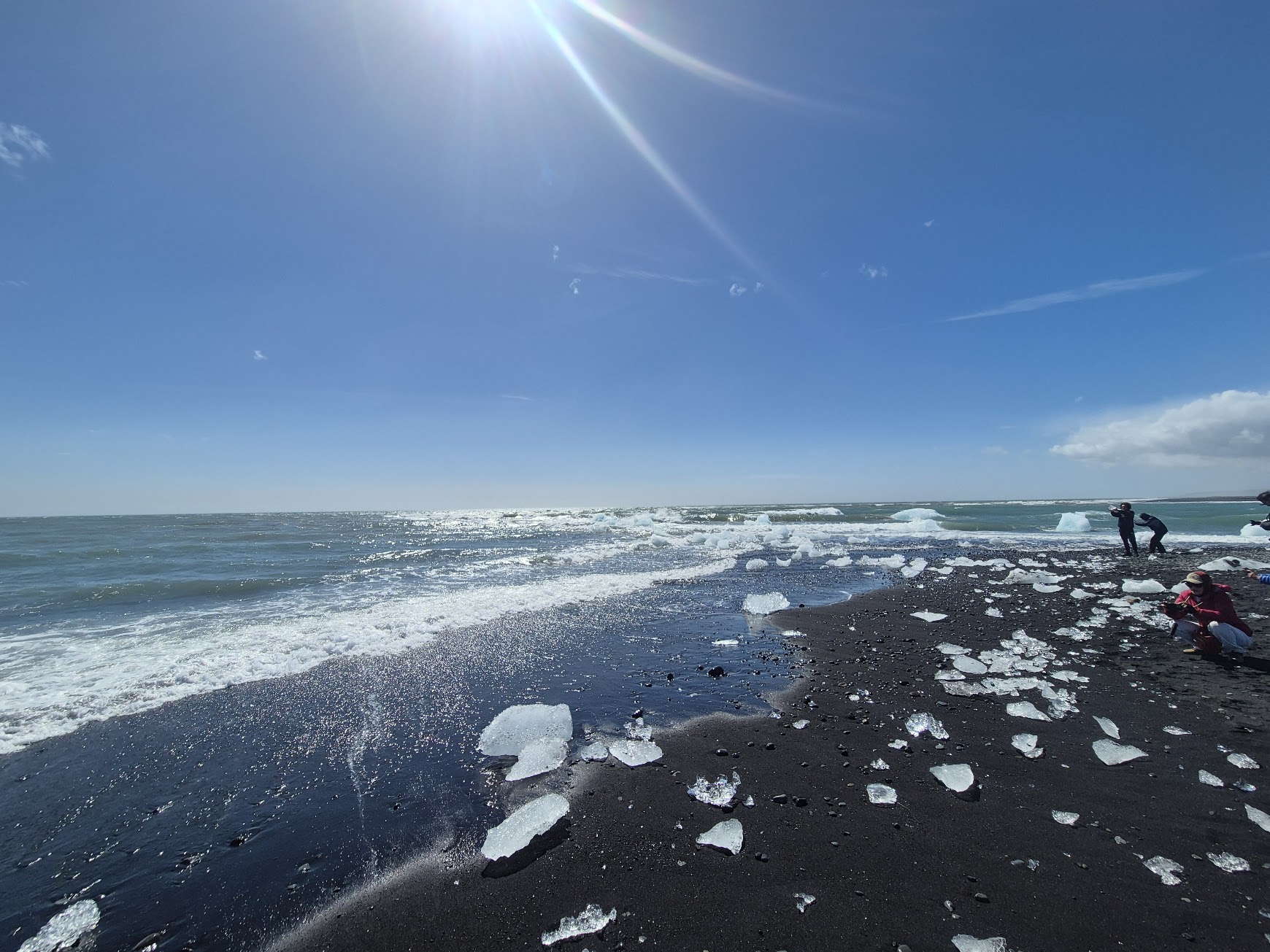 Clear ice chunks scattered across the black sand of Diamond Beach on a sunny day