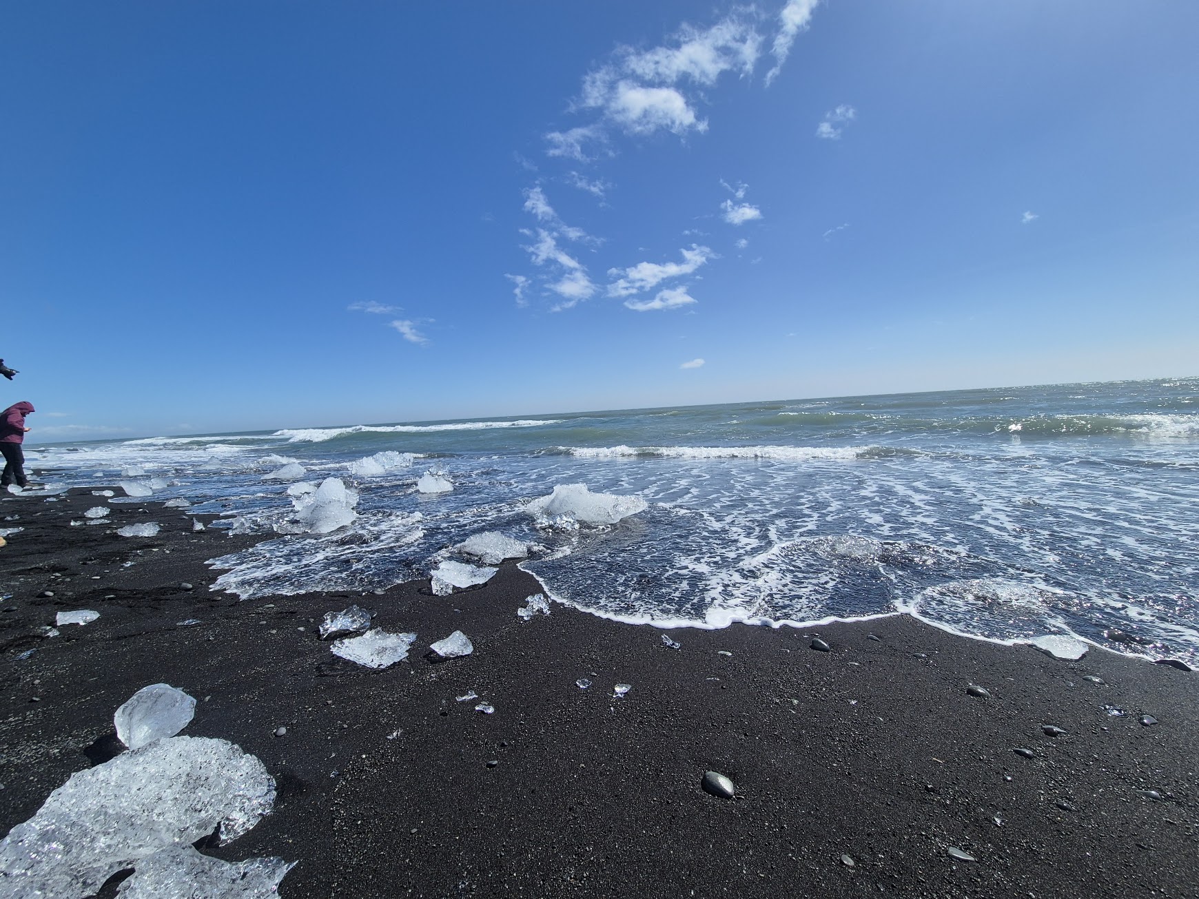 Waves washing over glassy ice fragments on the black sand at Diamond Beach
