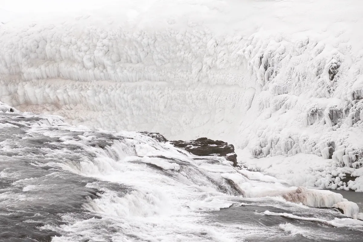 Gullfoss waterfall in winter, with water flowing between snow- and ice-covered gorge walls