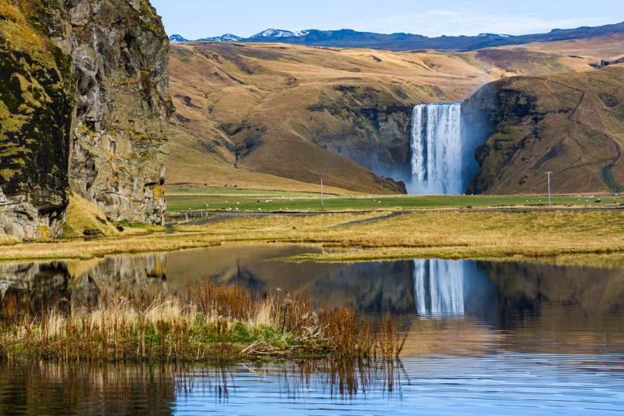 Skógafoss waterfall reflected in calm water on Iceland's South Coast
