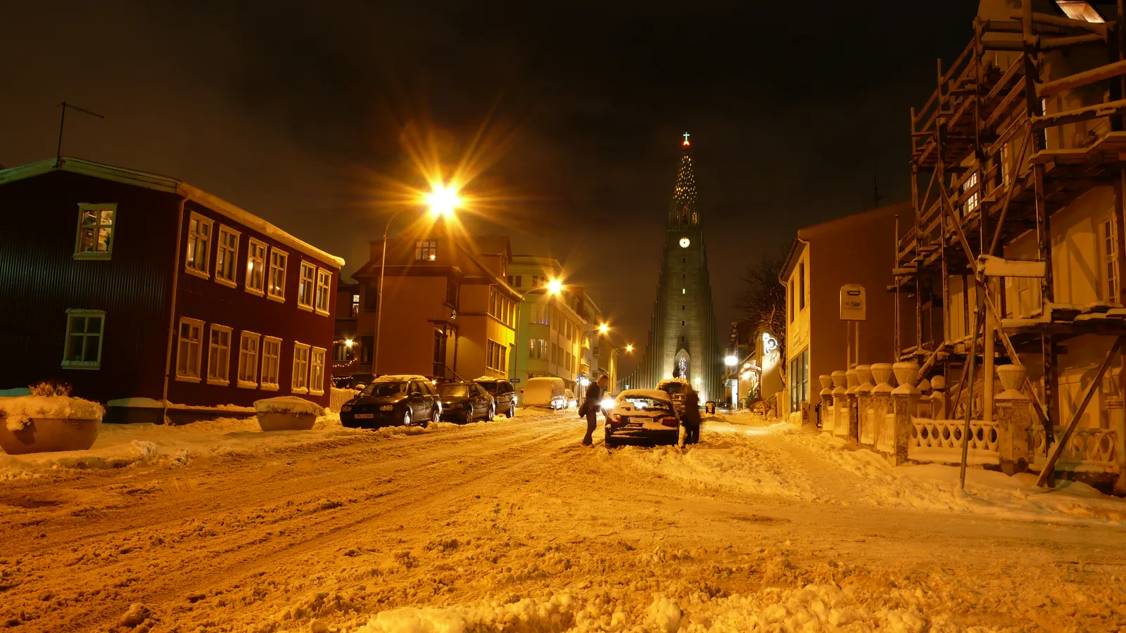 Snow-covered Reykjavík street at night under warm street lamps, with Hallgrímskirkja church lit at the end